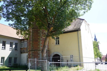 Syndikatshof Ein großes Gebäude mit Backsteinmauer und Torbogen, flankiert von einem hohen Baum und Zaun.