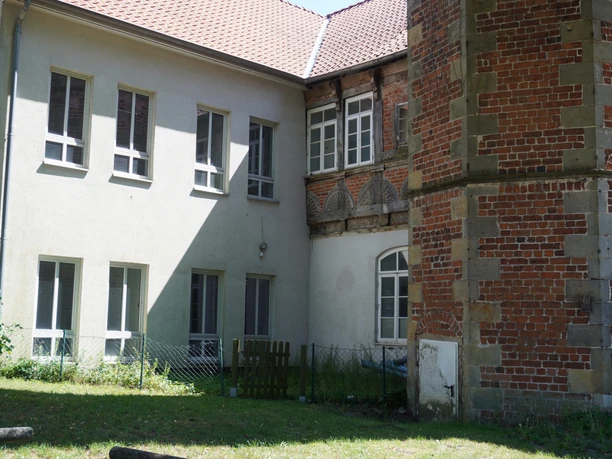 Zweigeschossiges Gebäude aus Backstein und verputztem Mauerwerk mit markantem Eckturm und Fenstern.