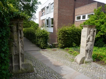 Steinskulpturen Wächtern gleich flankieren einen gepflasterten Weg, umgeben von dichter Vegetation.