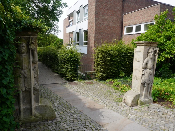 Steinskulpturen Wächtern gleich flankieren einen gepflasterten Weg, umgeben von dichter Vegetation.