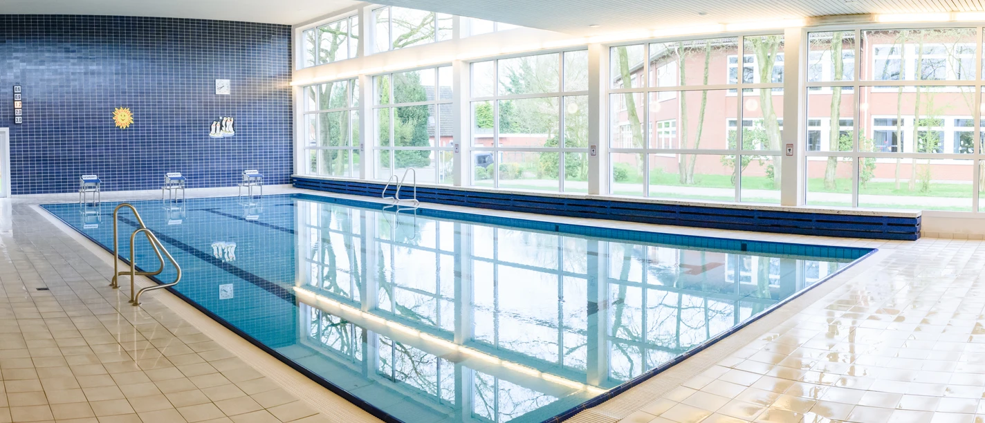 Schwimmbad Hesel Du erblickst das helle Hallenbad Hesel, dessen Wasser die breite Fensterfront klar reflektiert.