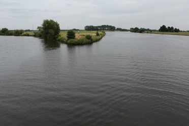 Mündung der Aller in die Weser mit ruhigem Wasser, grünen Ufern und leicht bewölktem Himmel.