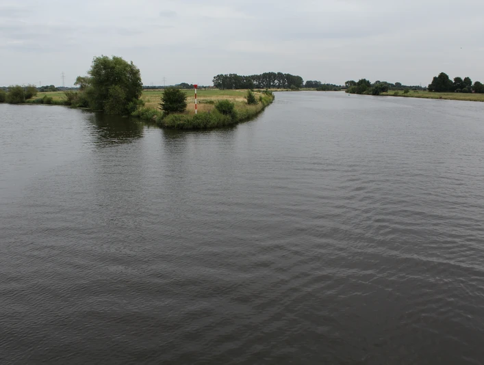 Mündung der Aller in die Weser mit ruhigem Wasser, grünen Ufern und leicht bewölktem Himmel.
