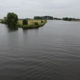 Allermündung Mündung der Aller in die Weser mit ruhigem Wasser, grünen Ufern und leicht bewölktem Himmel.