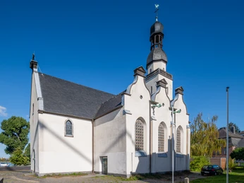 Saint Clemens Die Sankt Clemens Kirche ist ein weißes, historisches Gebäude mit markantem Turm und schmuckvollen Fenstern. Links sind Bäume und blauer Himmel zu sehen.St. Clement's Church is a white, historic building with a striking tower and ornate windows. Trees and blue sky can be seen on the left.