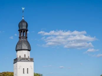 Saint Clemens Barocker Kirchturm von St. Clemens vor strahlend blauem Himmel mit leichten Wolkenformationen.Baroque church tower of St. Clemens in front of a bright blue sky with light cloud formations.
