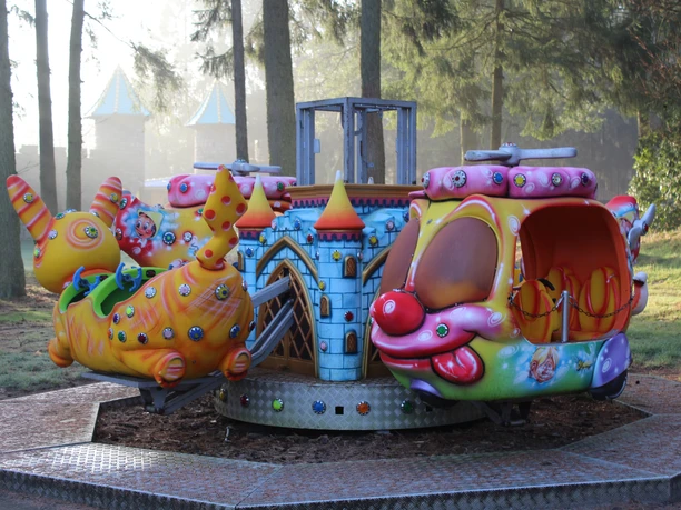 A colorful carousel with child-friendly animal figures stands in the shady forest of Magic Park Verden.