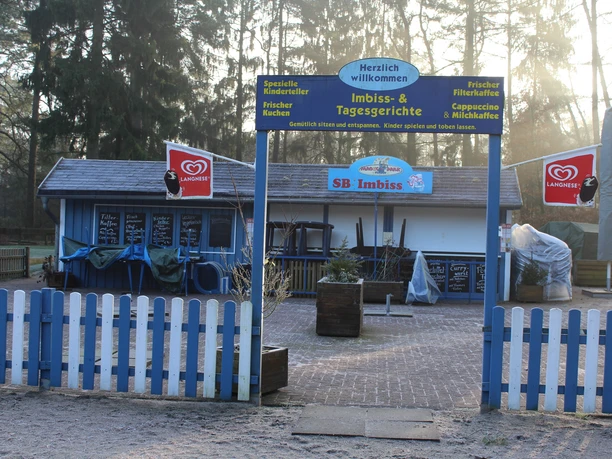 A blue and white painted outdoor snack bar, surrounded by trees and a sandy path, invites you to linger with child-friendly food and drinks.