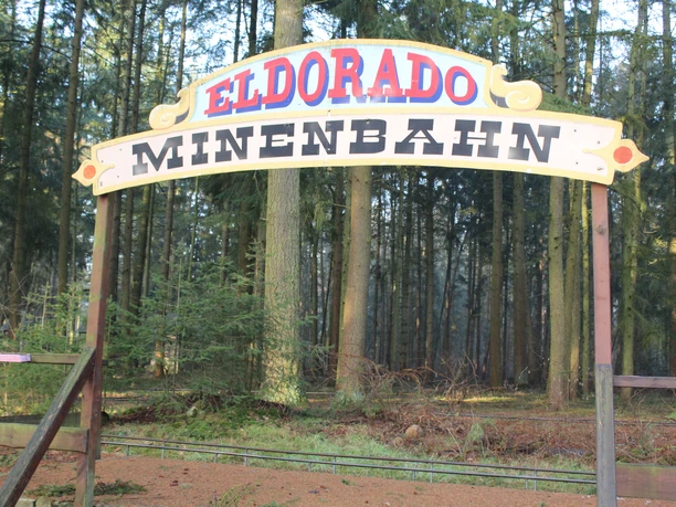Magic Park Verden Sign with the inscription "Eldorado Mine Train" in front of a dense coniferous forest in Magic Park Verden.