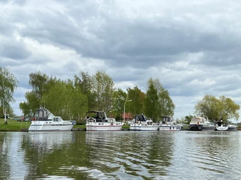 Verdener Motorbootverein Eine Reihe von Motorbooten liegt an einem ruhigen Flussufer, gesäumt von Bäumen unter bewölktem Himmel.