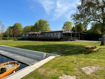 Wassersportverein Verden an einem sonnigen Tag, mit großem Rasen, Bootsanleger und Picknicktisch.