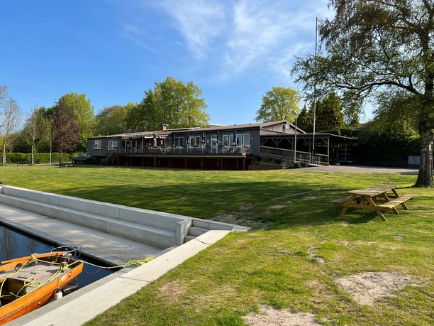 Wassersportverein Verden an einem sonnigen Tag, mit großem Rasen, Bootsanleger und Picknicktisch.