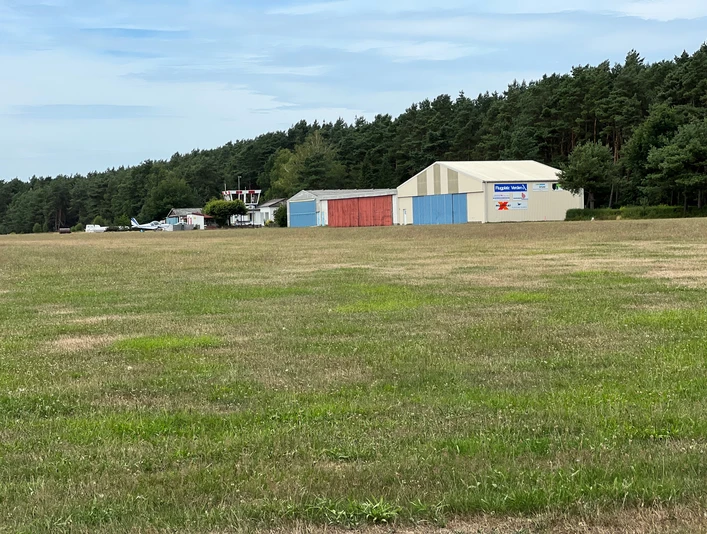 Ein kleiner Flughafen mit angrenzenden Hangars und einem Wald im Hintergrund bei Verden, Scharnhorst.