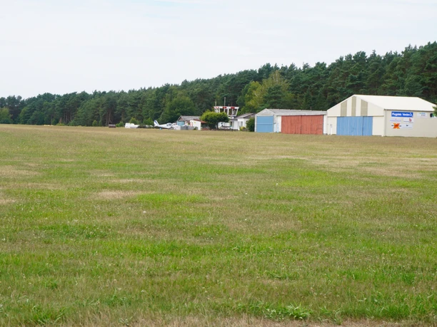 Flughafen Verden Scharnhorst Flughafen Verden Scharnhorst: Weite Wiese, Hangar-Gebäude mit kleinen Flugzeugen im Hintergrund.