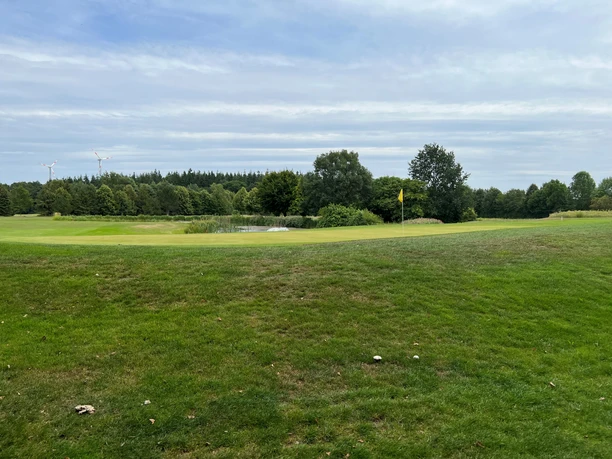 Spacious grass course at Verden Golf Club with surrounding trees and wind turbines on the horizon.