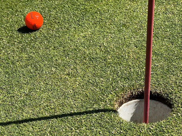 Golfloch Golfball auf einem gepflegten Grün nahe dem Loch, mit einem teilweise sichtbaren Flaggenstock.