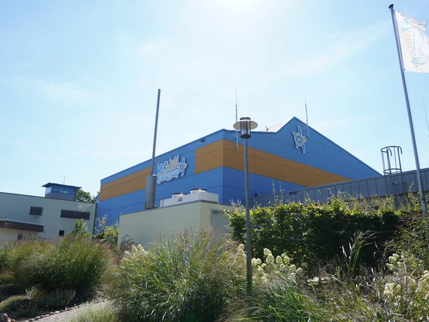 Wellnessbad mit markant blauer und oranger Fassade, umgeben von blühenden Gräsern bei klarem Himmel.