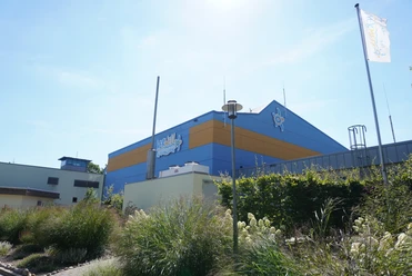 Verwell Verden Wellnessbad mit markant blauer und oranger Fassade, umgeben von blühenden Gräsern bei klarem Himmel.