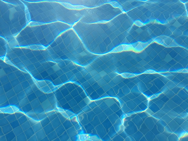 Kacheln unter klarem Wasser, reflektieren Sonnenlicht im Schwimmbad; blaues Muster sichtbar.