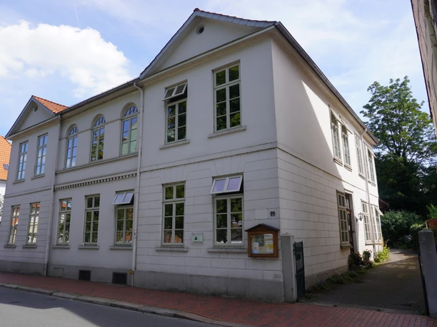 A two-story, white residential building with a gabled roof and many windows on a quiet street.