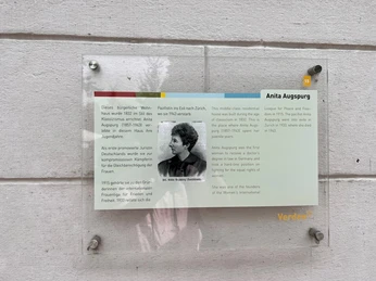 Glasplatte an einer weißen Wand mit Text über Anita Augspurg, erste promovierte Juristin Deutschlands.