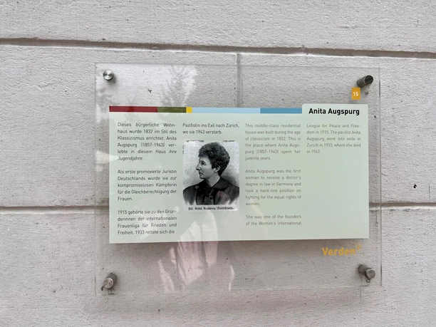 Glasplatte an einer weißen Wand mit Text über Anita Augspurg, erste promovierte Juristin Deutschlands.