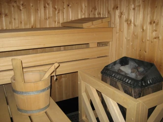 Sauna mit hölzernem Eimer und Schöpfkelle, Holzwänden und Heizofen mit Steinen in einem gemütlichen Raum.