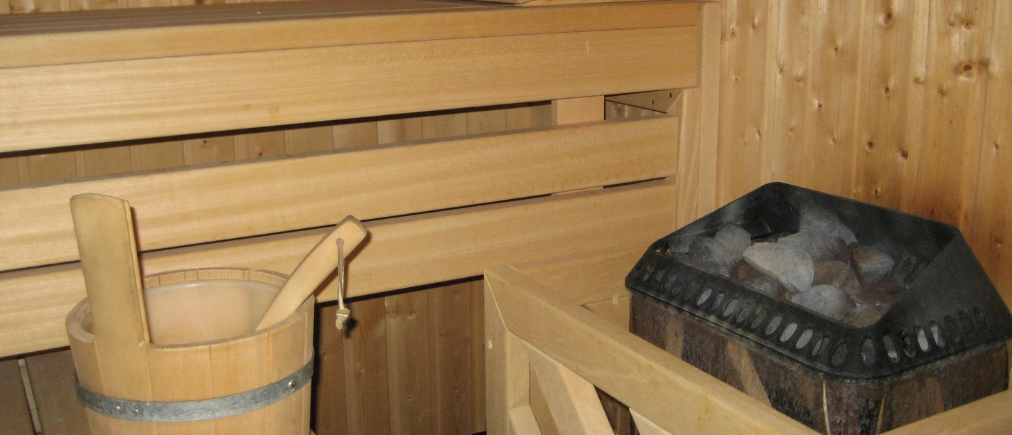 A sauna with a wooden bucket and ladle, wooden walls, and a stone-heated stove in a cozy room.