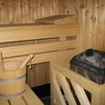 Sauna Sauna mit hölzernem Eimer und Schöpfkelle, Holzwänden und Heizofen mit Steinen in einem gemütlichen Raum.