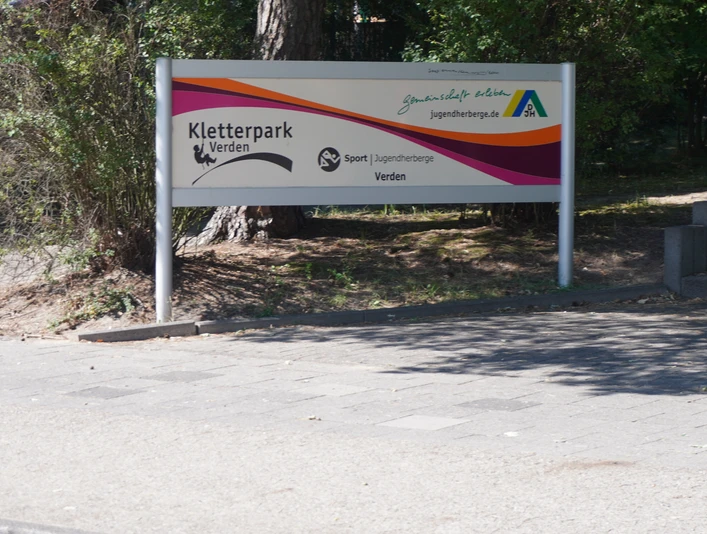 Kletterpark Verden Schild am Eingang des Kletterparks Verden, umgeben von Bäumen und Wegen.Sign at the entrance to the Verden climbing park, surrounded by trees and paths.Skilt ved indgangen til Verden klatrepark, omgivet af træer og stier.Bord bij de ingang van het klimpark Verden, omgeven door bomen en paden.