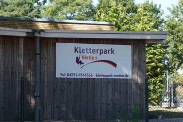 Kletterpark Verden Holzgebäude mit Schild des Kletterparks Verden, umgeben von Bäumen, bietet Abenteuer und Natur.