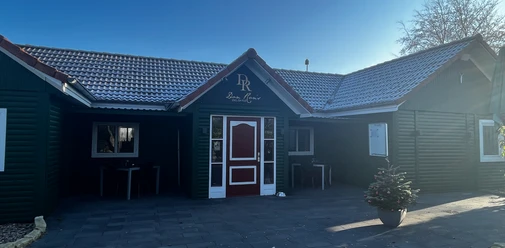Don Ron's English Pub Gemütliches englisches Pub mit dunkelgrüner Fassade und roten Akzenten, umgeben von klarer Natur.
