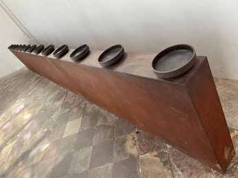 Das letzte Abendmahl Langgestreckter, minimalistisch gestalteter Tisch mit runden, schlichten Platten auf gemustertem Boden.