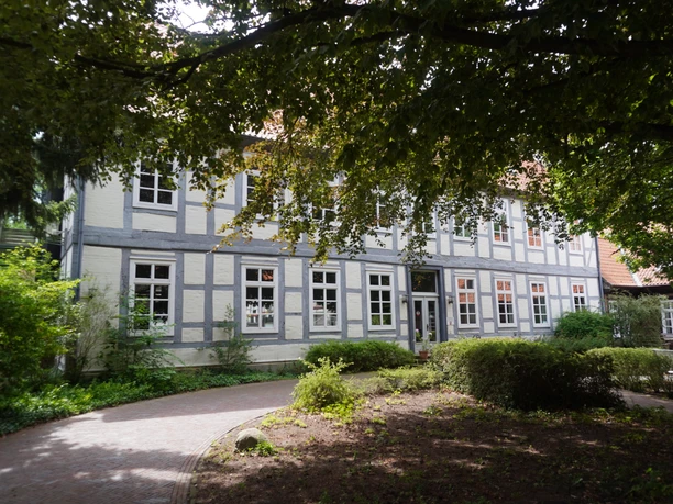 Museum Domherrenhaus A two-storey half-timbered house with white walls, surrounded by trees and a path in the foreground.