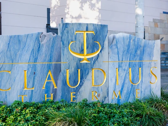 Claudius Therme Das Bild zeigt das stilisierte Logo der Claudius-Therme auf einer grau-blauen, schlichten Steintafel. Die goldene Schrift hebt sich elegant ab und vermittelt einen Eindruck von Entspannung und Luxus.The picture shows the stylized logo of the Claudius-Therme on a grey-blue, simple stone plaque. The golden lettering stands out elegantly and conveys an impression of relaxation and luxury.