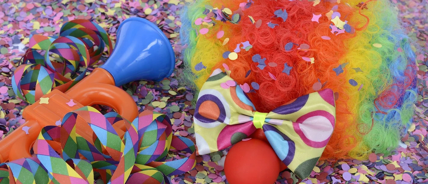 Karneval in Bad Driburg Buntes Karnevalszubehör, inklusive Clownsperücke, Tröte und Schleife, umgeben von Konfetti.
