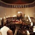 Piuskirche_Wiedenbrück.jpg Eine festliche Weihnachtsmesse in einer Kirche mit großen Kronleuchtern, geschmückten Tannenbäumen und Menschen.