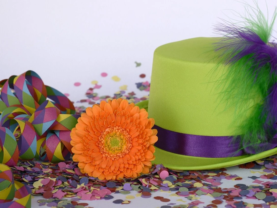 Karneval in Bad Driburg Grüner Hut mit lila Band und orangener Gerbera, umgeben von buntem Konfetti und Luftschlangen.