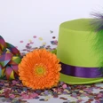 Karneval in Bad Driburg Grüner Hut mit lila Band und orangener Gerbera, umgeben von buntem Konfetti und Luftschlangen.