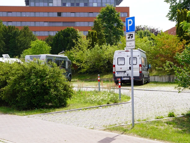 RV parking spot in Verden with a paved surface, surrounded by trees, and a parking sign.