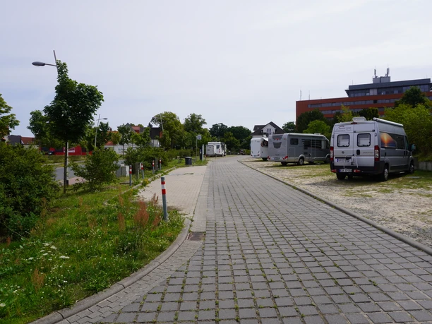 A RV parking area with a paved path and trees surrounding it, with several parked RVs in the background.