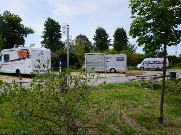 Wohnmobilstellplatz Verden Wohnmobilstellplatz Verden mit mehreren Fahrzeugen auf gepflastertem Boden, umgeben von Bäumen.