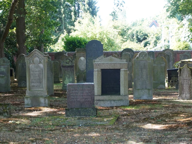 Eine ruhige, historische Begräbnisstätte mit alten Grabsteinen unter schattenspendenden Bäumen.