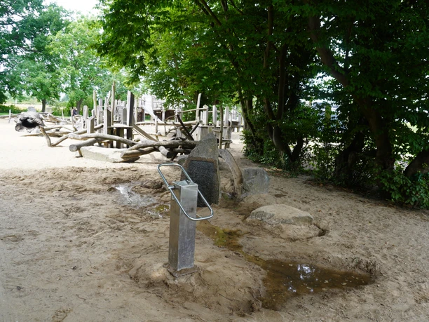 Kinderspielplatz Allerpark Verden Naturbelassener Spielplatz in Verden mit Holzgeräten zum Klettern, Sandfläche und umliegenden Bäumen.