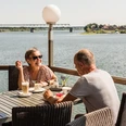 Eine Frau und ein Mann sitzen auf der Terasse im "Cafe von Herzen" in Lauenburg. Die Sonne scheint und sie blicken direkt auf die Elbe während sie Kaffee und Kuchen genieĂŸen.
