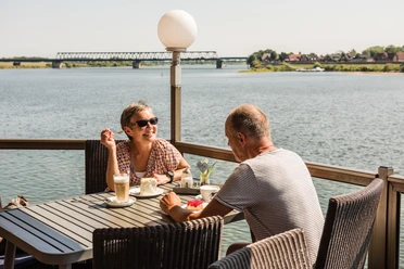 Im Cafe von Herzen in Lauenburg mit Elbblick Eine Frau und ein Mann sitzen auf der Terasse im "Cafe von Herzen" in Lauenburg. Die Sonne scheint und sie blicken direkt auf die Elbe während sie Kaffee und Kuchen genießen.