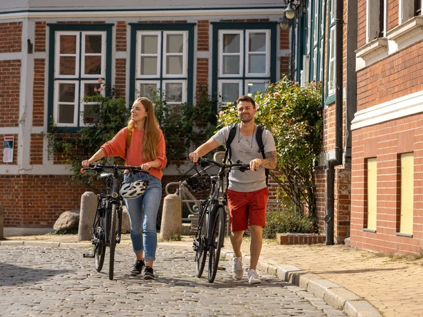 Paar mit Fahrrädern in Stadt Lauenburg Ein Paar schiebt ihre Fahrräder durch die Stadt Lauenburg. Im Hintergrund ist ein Gebäude der historischen Altstadt zu sehen.