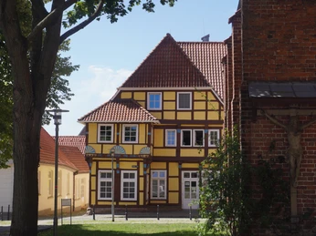 Bürgerhaus 1561 Fachwerkhaus von 1561 mit gelben Wänden und roten Dächern, flankiert von Bäumen, sonniger Tag.