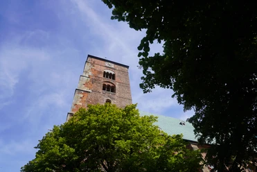 Dom Verden Gotisches Bauwerk mit imposantem Turm, umgeben von grünen Bäumen, unter strahlend blauem Himmel.