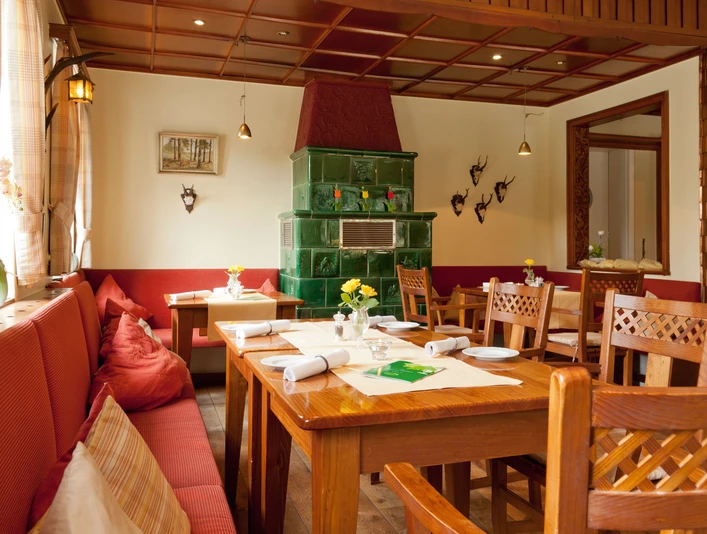 Hirschsprung_Foersterstube.jpg Rustikal eingerichteter Gastraum mit Holzstühlen und grünem Kachelofen, dekoriert mit Hirschgeweihen.